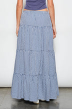 Person wearing a blue tiered skirt and purple top on a white background