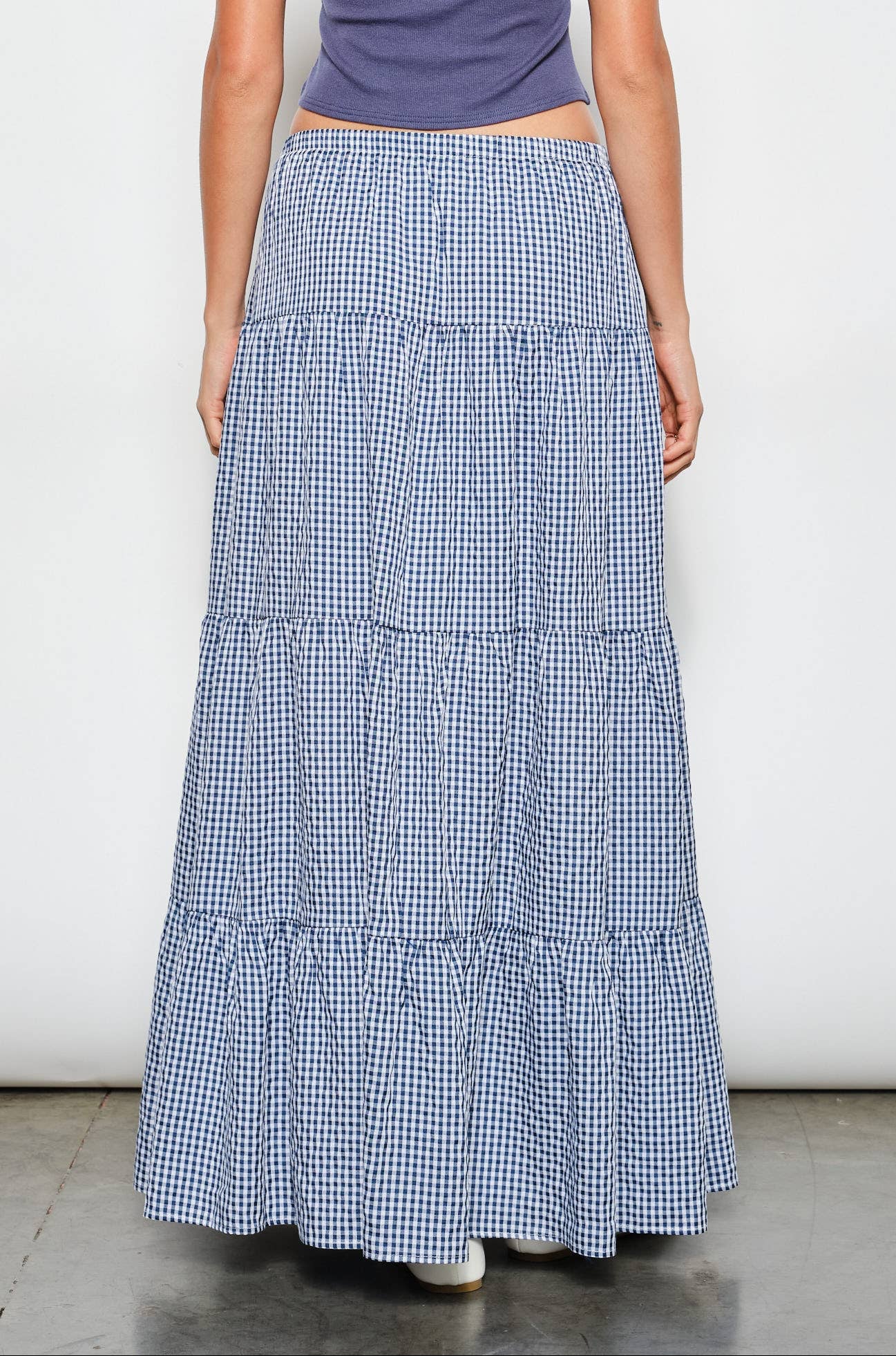 Person wearing a blue tiered skirt and purple top on a white background