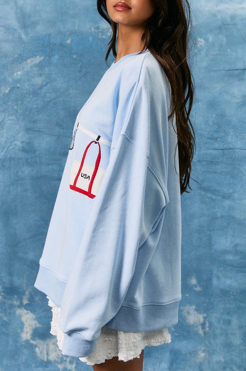 Woman wearing a light blue oversized sweatshirt with a graphic design against a textured blue wall.