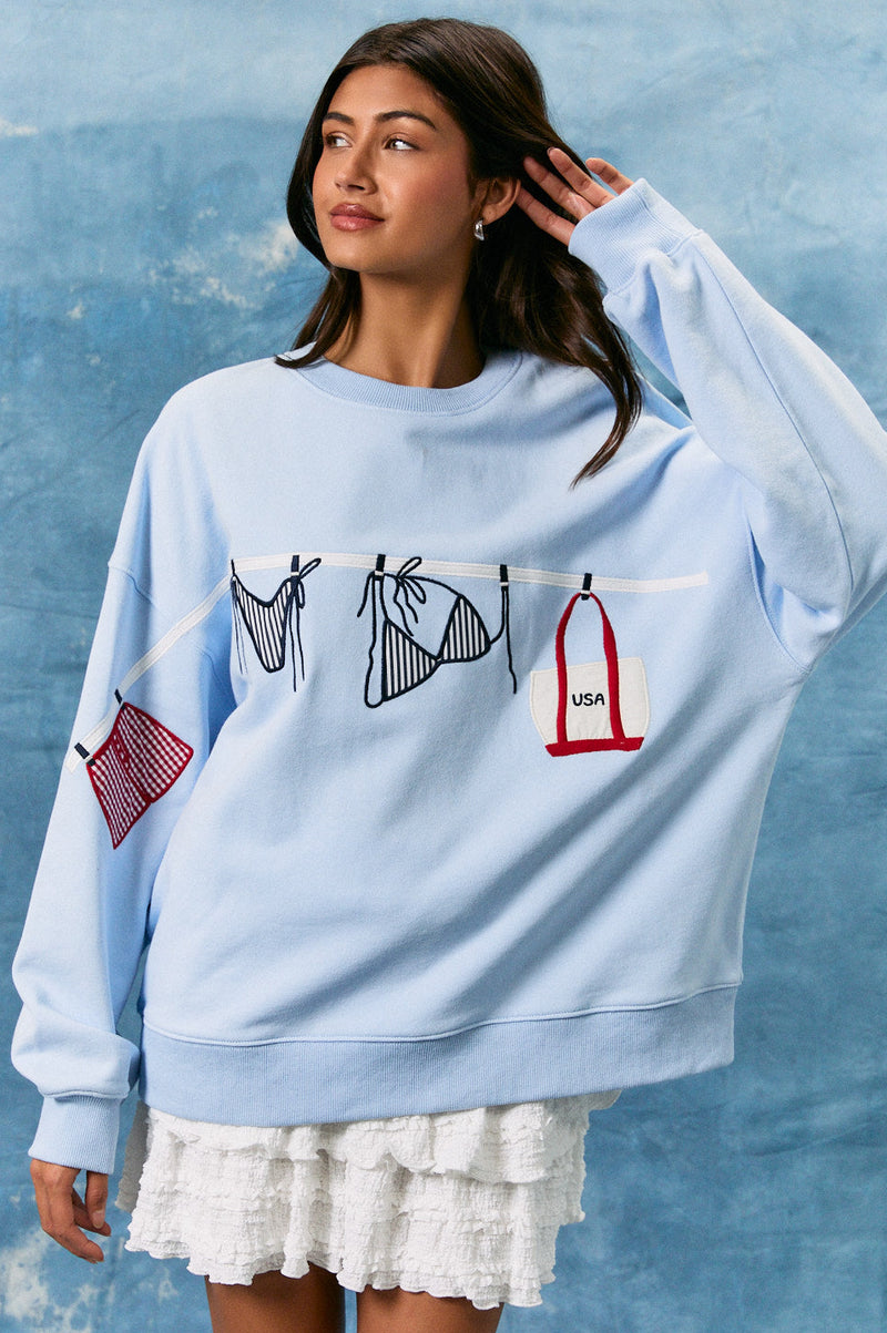 Woman wearing a light blue sweatshirt with graphic designs against a textured blue background