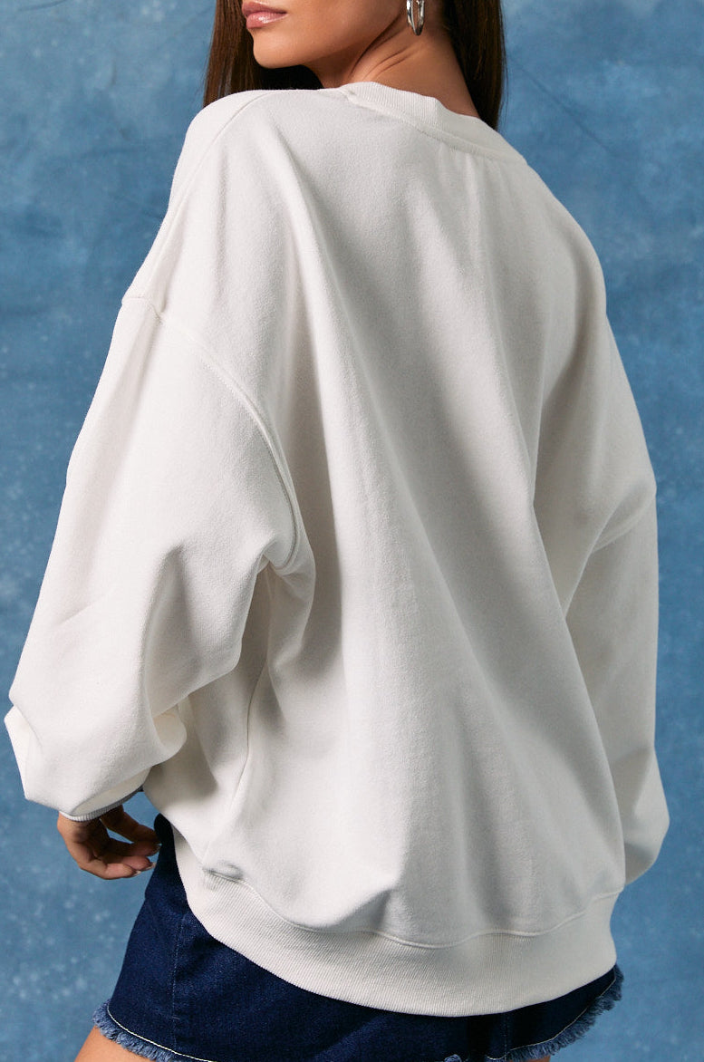 Woman wearing a white oversized sweatshirt and denim shorts against a blue textured background