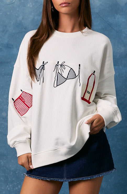 Woman wearing a white sweatshirt with graphic designs, denim skirt, and white boots against a blue background