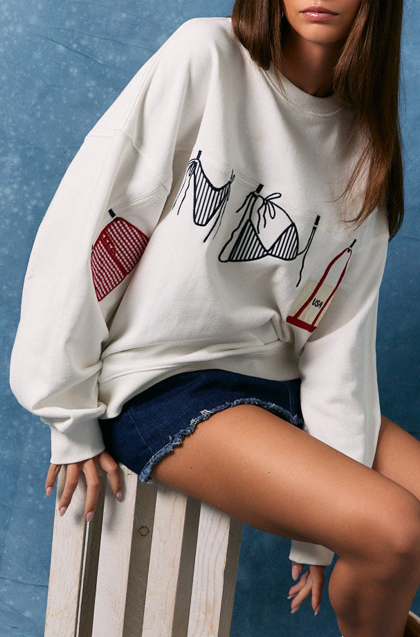 Woman wearing a white sweatshirt with graphics, denim shorts, and white boots against a blue background.