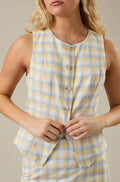 Yellow and blue plaid vest being buttoned by a person on a neutral background