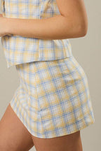 Woman wearing a yellow and blue checkered skirt against a beige background