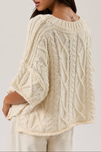 Woman wearing a cream knitted sweater against a plain background