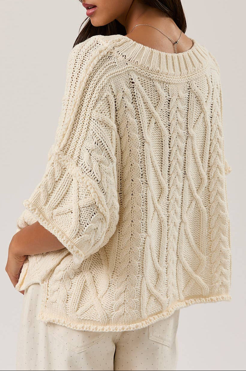 Woman wearing a cream knitted sweater against a plain background