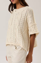 Woman wearing a cream-colored knitted top against a plain background
