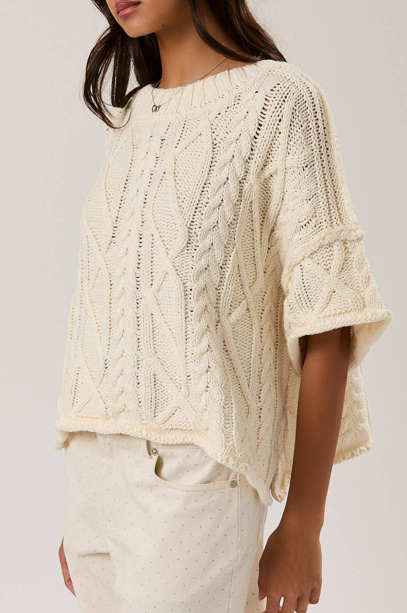 Woman wearing a cream-colored knitted top against a plain background