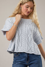Woman wearing a light blue knitted top and blue jeans against a plain background