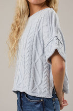 Woman wearing a light blue cable knit sweater and blue jeans against a beige background
