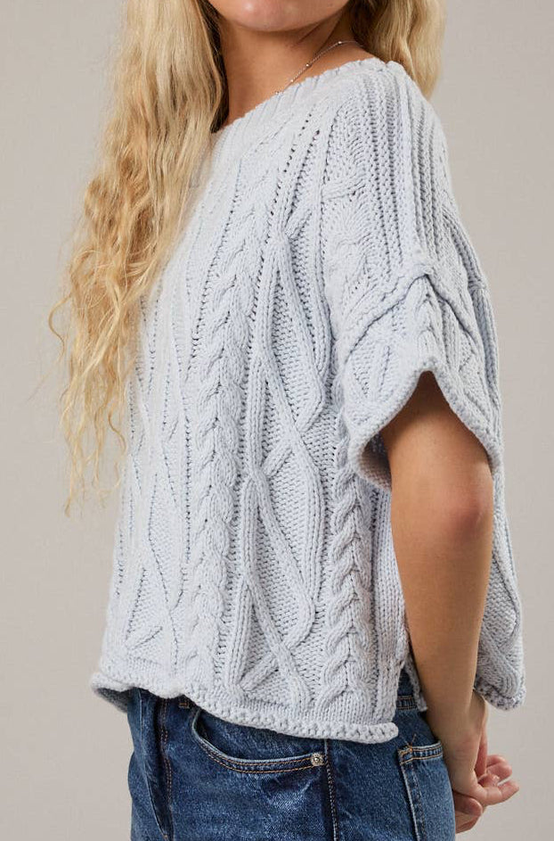 Woman wearing a light blue cable knit sweater and blue jeans against a beige background