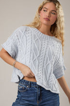 Woman wearing a light blue knitted top and blue jeans against a neutral background