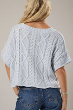 Person wearing a light blue knitted top and blue jeans on a beige background