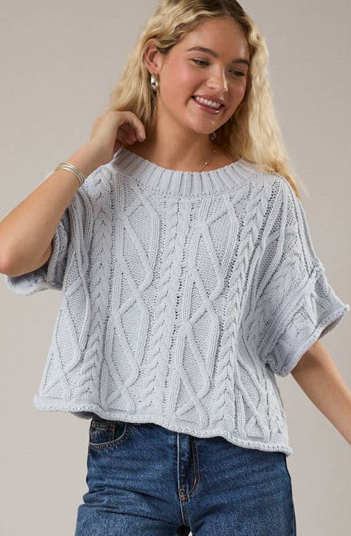 Woman wearing a light blue cable knit sweater and blue jeans on a beige background