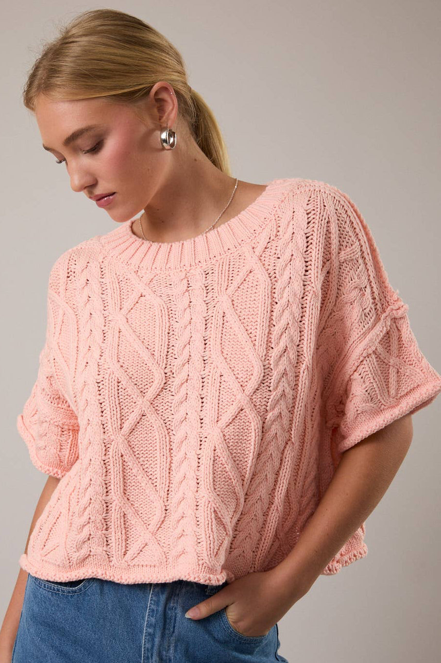 Woman wearing a pink knitted sweater and blue jeans against a gray background