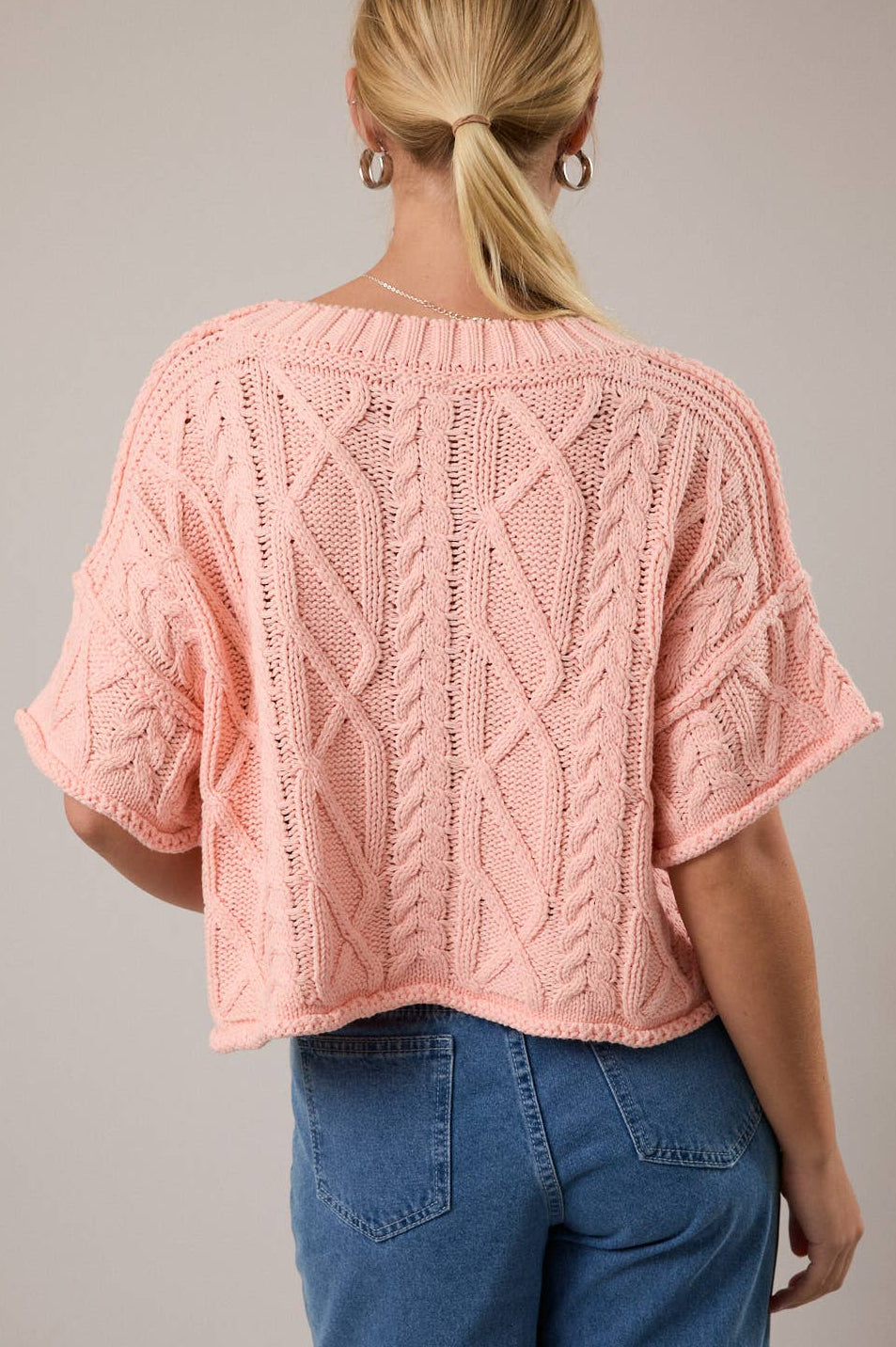 Person wearing a pink knitted top with a gray background
