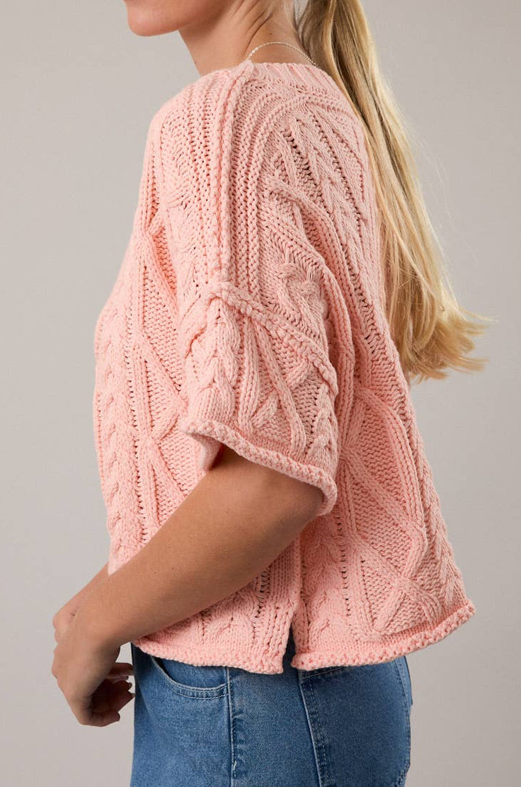 Woman wearing a pink knitted sweater and blue jeans against a plain background