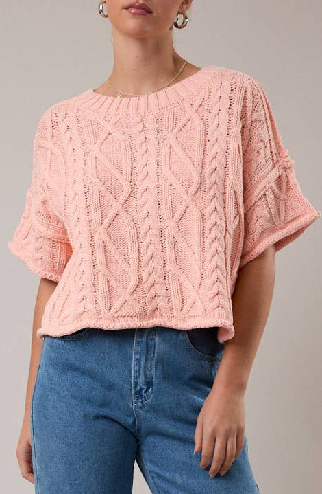 Woman wearing a pink cable knit sweater and blue jeans against a plain background