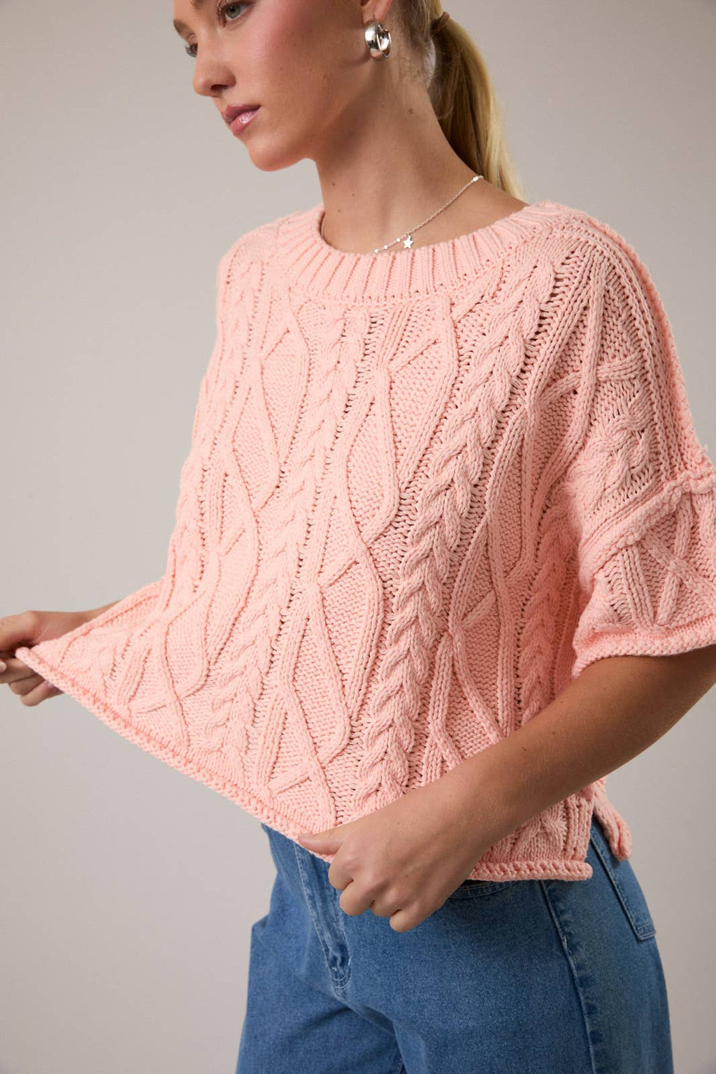 Woman wearing a pink knitted sweater with a gray background