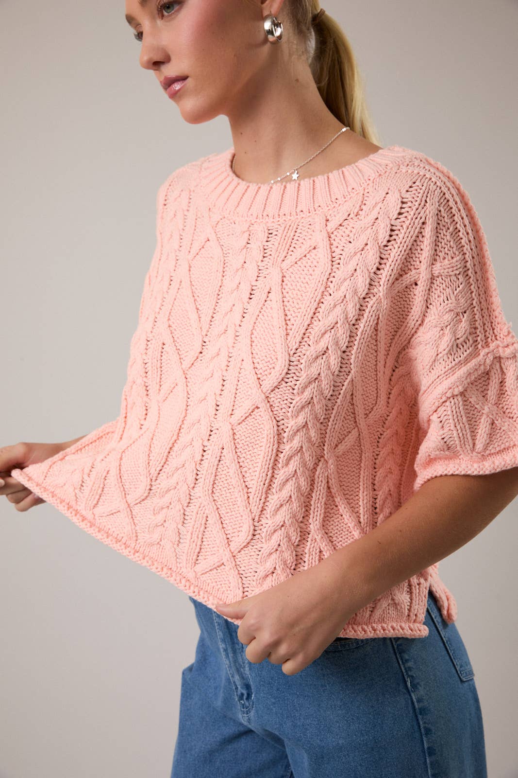 Woman wearing a pink knitted sweater with a gray background