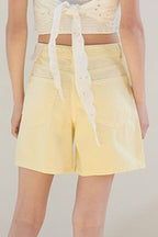 Person wearing a white lace top and yellow shorts on a plain background