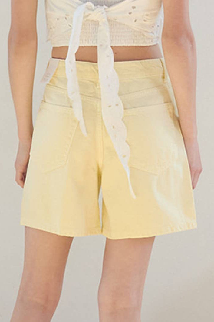 Person wearing a white lace top and yellow shorts on a plain background