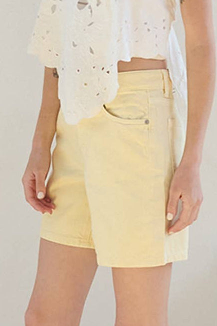 Woman wearing a white top and yellow shorts in a bright room.