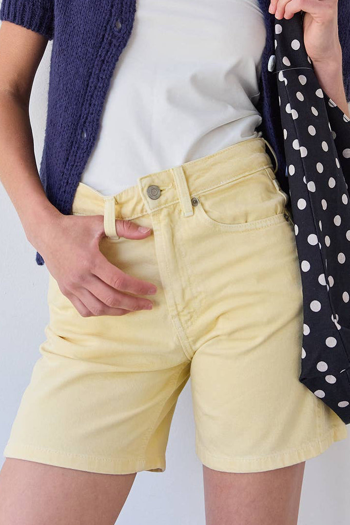 Woman wearing a white top, navy cardigan, and yellow shorts against a light background