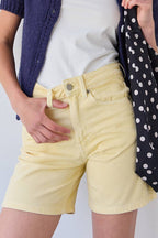 Woman wearing a white top, navy cardigan, and yellow shorts against a light background