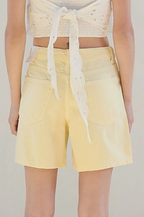 Woman wearing a white top and yellow shorts in a room with a neutral color scheme.