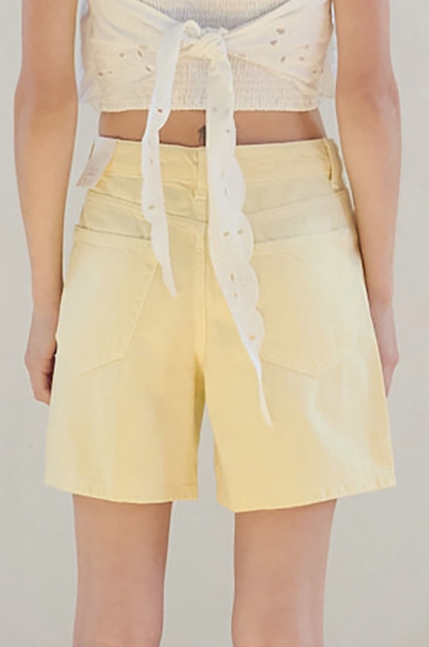 Woman wearing a white top and yellow shorts in a room with a neutral color scheme.