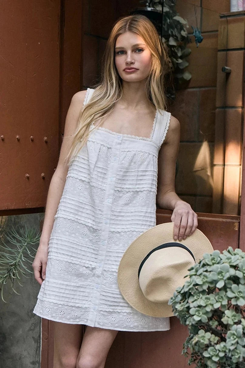 Woman in a white dress standing next to a door with plants around her.