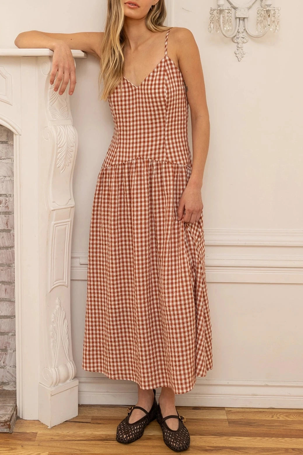 Woman wearing a rust and white checkered dress standing in a room with a fireplace.