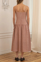 Woman wearing a checkered dress standing in a room with wooden floor and white walls.