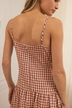 Woman wearing a rust and white checkered dress with thin straps.