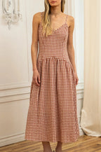Woman wearing a checkered dress standing in a room with white walls and wooden floor.