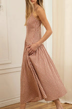 Woman wearing a rust and white checkered dress standing in a room with white walls and wooden floor.