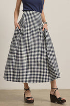 Woman wearing a navy top and navy and white checkered skirt against a neutral background