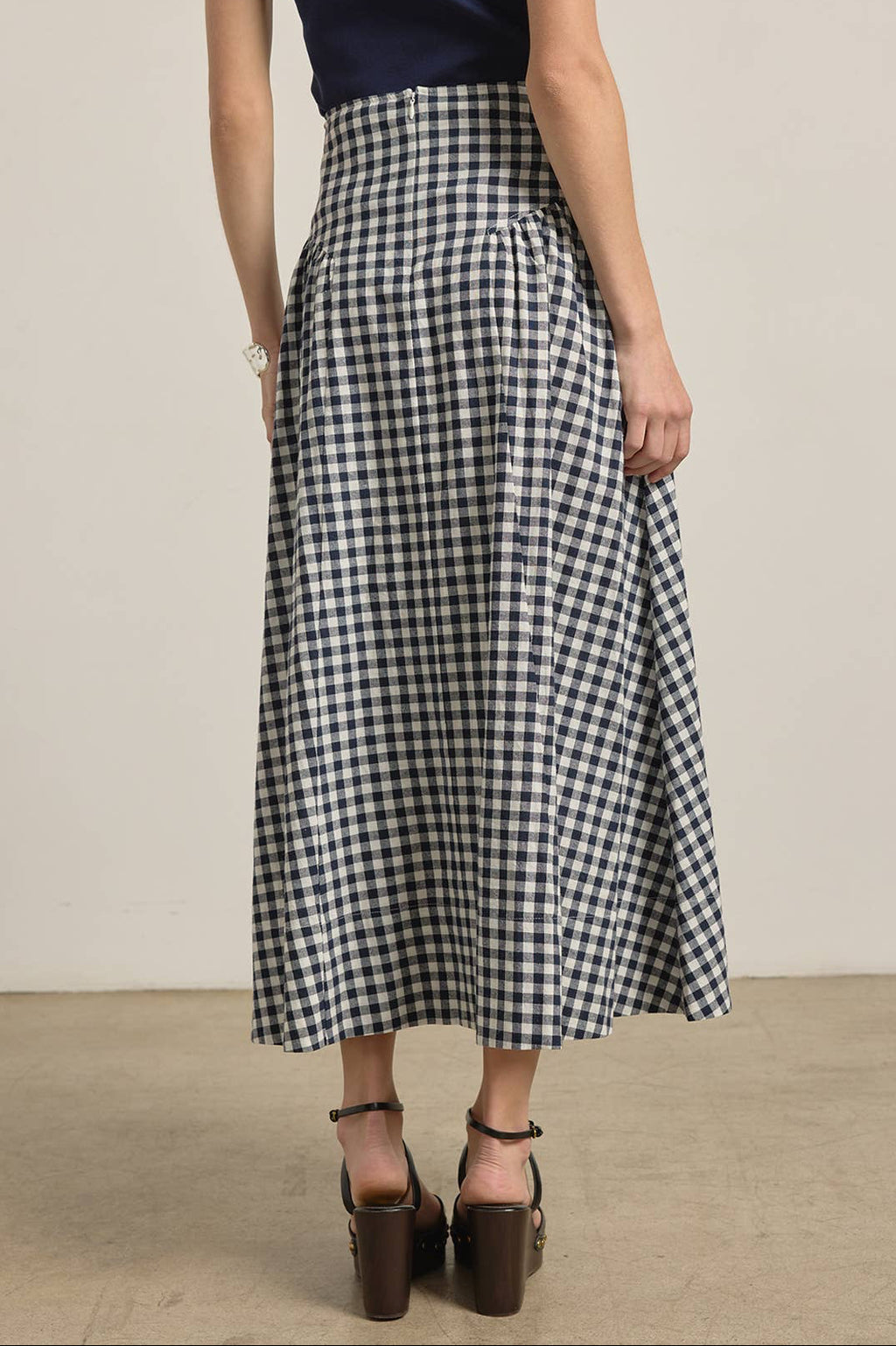 Person wearing a navy and white checkered skirt with a plain background