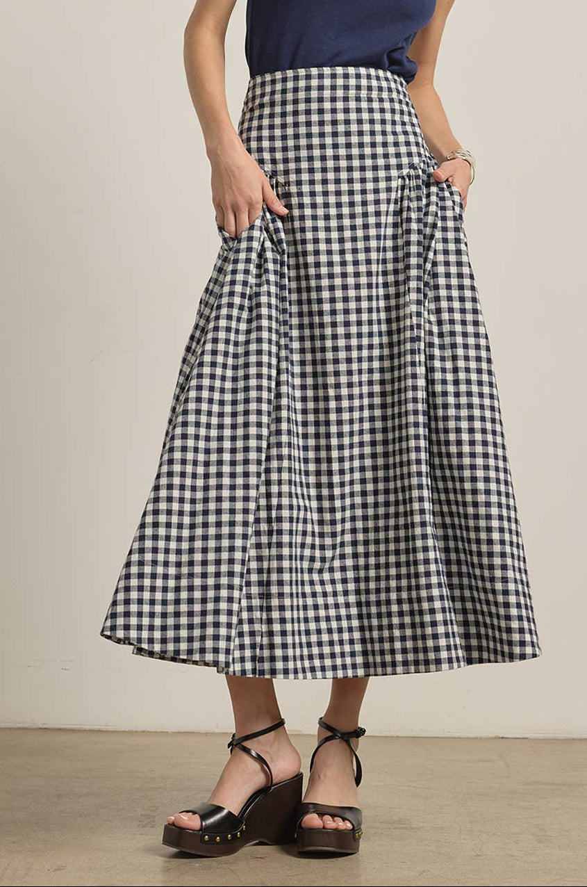 Woman wearing a blue top and gingham skirt against a neutral background