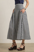 Woman wearing a navy top and navy and white checkered skirt on a plain background