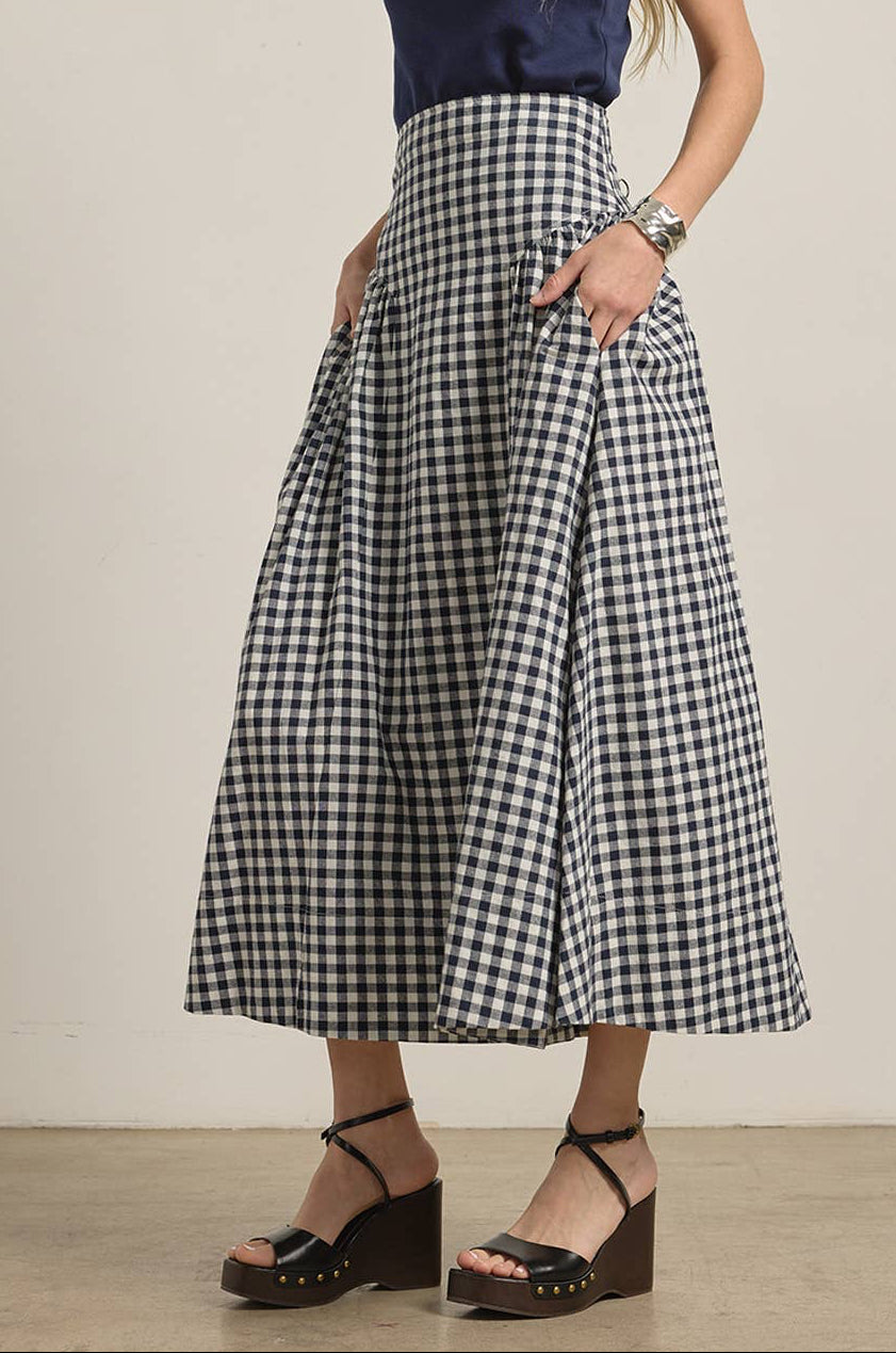 Woman wearing a navy top and navy and white checkered skirt on a plain background