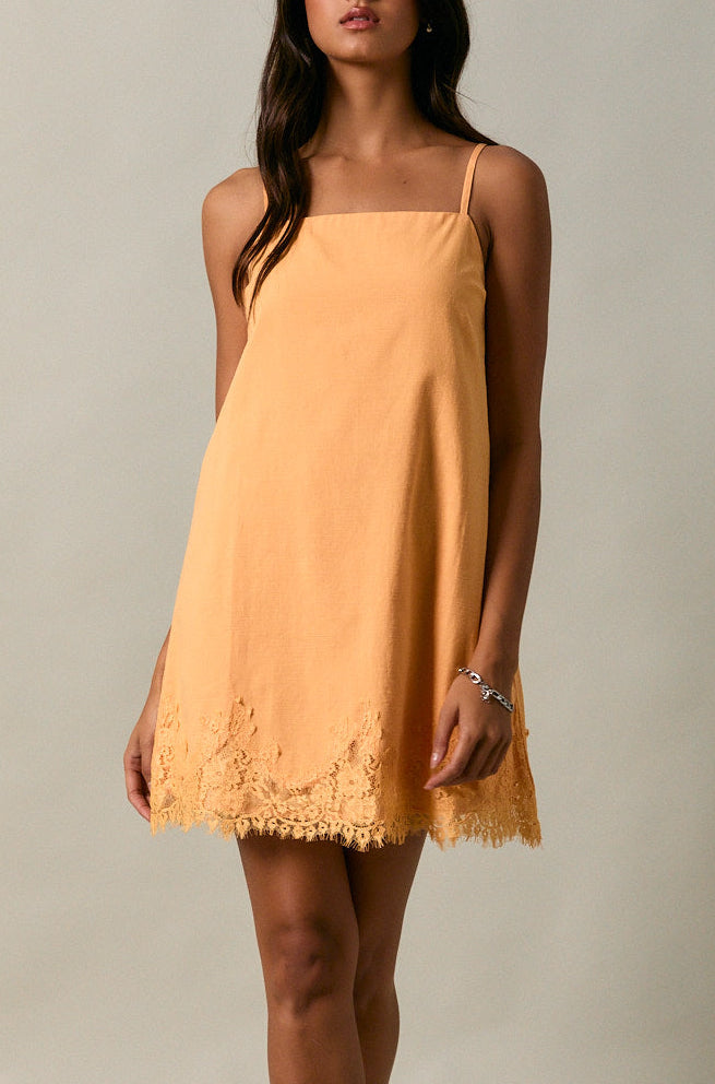 Woman wearing a mustard yellow dress with lace details on a plain background