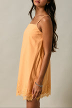 Woman wearing a light orange dress with thin straps against a neutral background