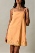Woman wearing a mustard yellow slip dress with lace trim against a neutral background