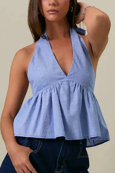 Woman wearing a blue top and denim shorts against a beige background