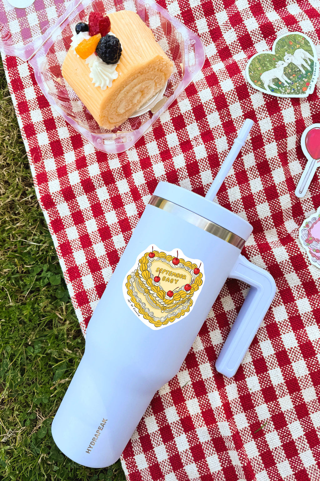 White tumbler with a cake design on a red and white checkered tablecloth with a dessert in the background.