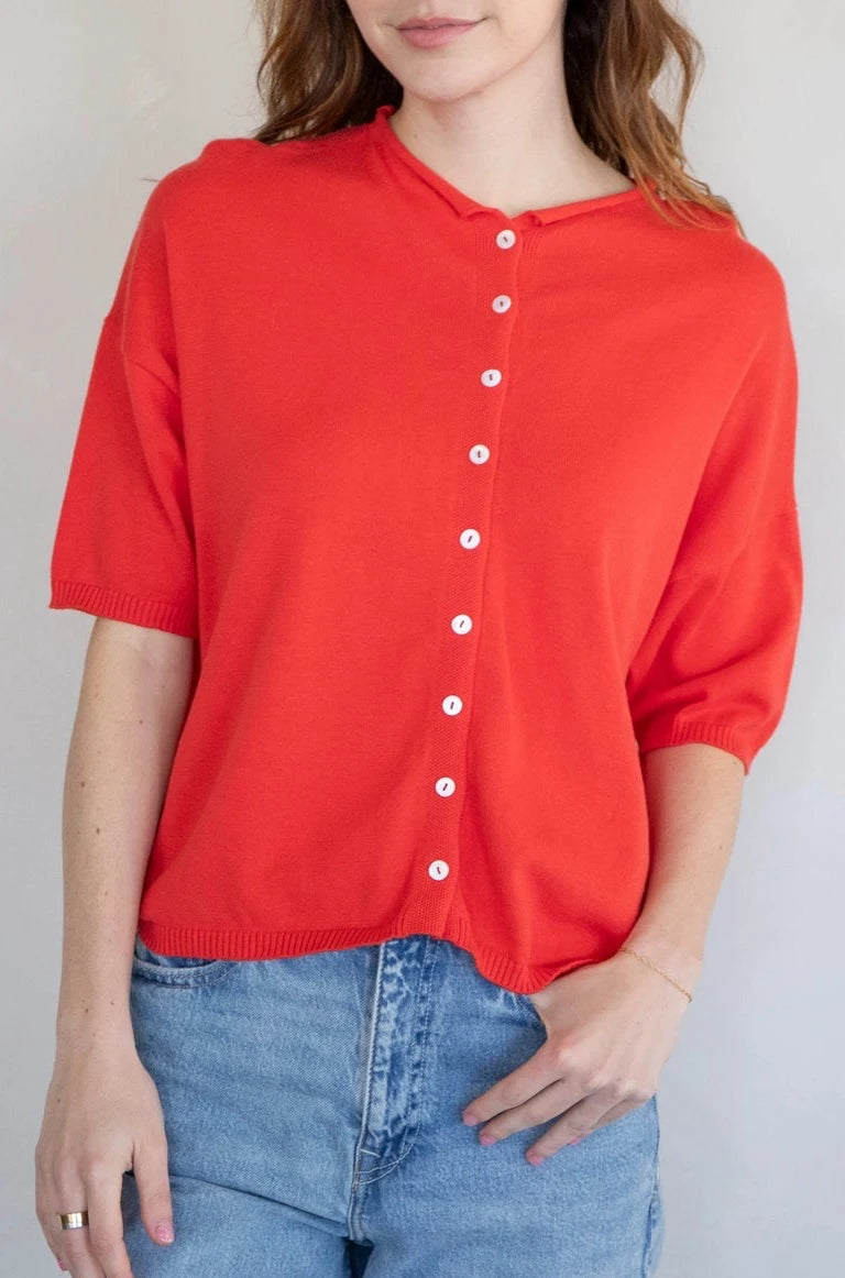 Woman wearing a red button-up shirt and blue jeans against a plain background