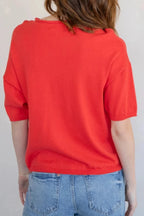 Person wearing a red shirt and blue jeans against a white wall